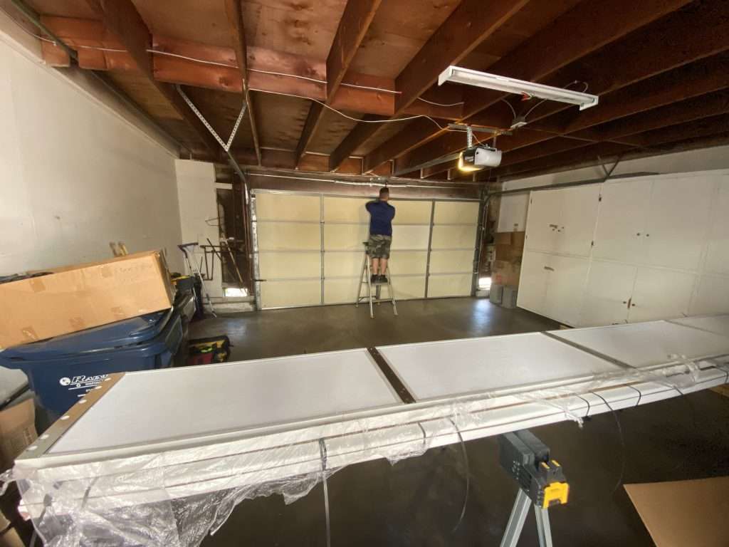 Garage Door Repair vs Replacement: How to Know What’s Best for Your Home 3 Garage door professional installing or repairing a sectional garage door inside a residential garage with exposed ceiling beams and mounted garage door opener.