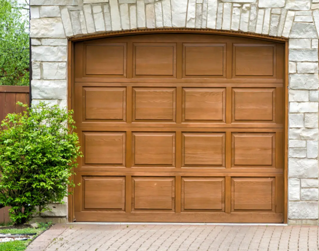 Wood garage door with raised panel design installed in a stone garage entrance, demonstrating how replacing garage door can enhance home efficiency, insulation, and natural curb appeal.