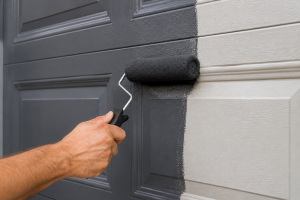 Closeup hand painting garage door with a foam roller for a smooth finish without brush marks on a modern residential garage door exterior.