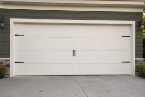 White residential sectional garage door with decorative black hinges and handles, installed on a modern home with stone accents and a concrete driveway, showcasing durable garage door hardware and curb appeal.