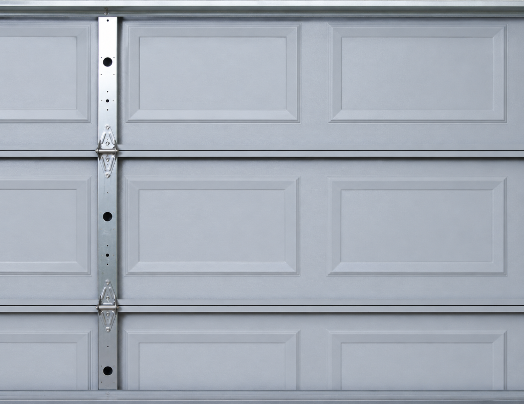 Close-up view of metal garage door hinges connecting sectional panels on a cool gray residential garage door, highlighting the hardware that supports smooth garage door movement and structural stability.