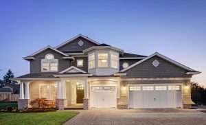 Luxurious two-story home with elegant architecture, illuminated exterior lighting, and white carriage-style garage doors at twilight. This upscale residential property features a spacious driveway, covered front porch, landscaped yard, and modern garage door design, showcasing premium curb appeal and luxury home aesthetics.