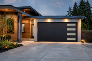 A modern house featuring a sleek black modern garage door with clean architectural lines, warm exterior lighting, and a spacious concrete driveway, showcasing contemporary residential garage door design.