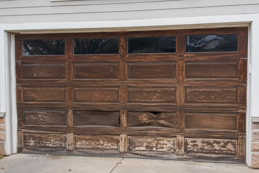 Repair of Wood Look Garage Doors for Residential Homes 2 Weathered wood-look garage door with visible scratches, chipped finish, fading, discoloration, and dented panels, showing common signs that a wood look garage door needs repair to restore curb appeal and durability.